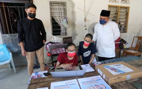 Ahmad Azri (kanan) menyampaikan laptop kepada Ahmad (dua dari kanan) dan Muhammad (dua kiri) di Kampung Tengah Puchong, Subang Jaya pada Jumaat.