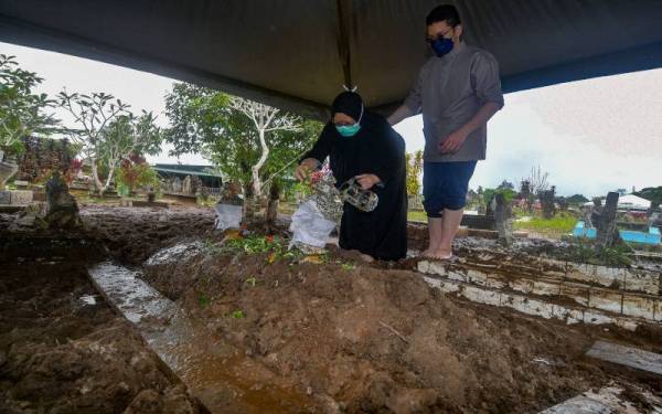 Dayang Farezah Abang Mustapha ditemani anaknya Hazim Izzuddin Jumaat (kanan) menyiram air di pusara bapa saudaranya, Mohamad Jemuri di Tanah Perkuburan Islam Kampung Pinang Jawa, pada Rabu. Foto Bernama
