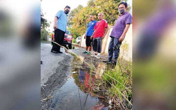 Asrul Nizan (kiri) meninjau keadaan jalan di hadapan Dewan Kospen Kampung Sena digenangi air yang terhasil akibat kebocoran paip air.