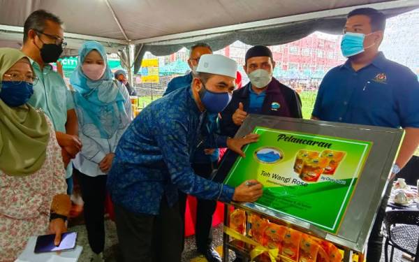 Nik Muhammad Zawawi menandatangani plak perasmian produk tempatan di Program Jualan Keluarga Malaysia (PJKM) di Bandar Baharu Pasir Puteh pada Sabtu.