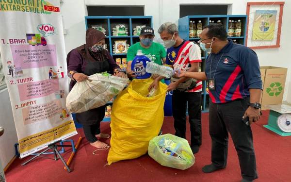 Penduduk PPR Beringin, Kepong (dari kiri) Che Roziani Mohd Shariff, Mohd Osman Shariff dan Mohd Azuan Othman menyerahkan barangan kitar semula kepada petugas Dewan Bandaraya Kuala Lumpur untuk ditukarkan kepada barangan keperluan asas di Kios 1 Community 1 Recycle (1C1R). - Foto Bernama