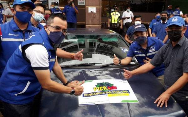 Asyraf Wajdi (tengah) menampal pelekat sebagai simbolik perasmian program Pick Kids Pengangkutan Awam Percuma Khusus Untuk Penduduk Pasir Gudang di Pejabat UMNO Bahagian Pasir Gudang, Bandar Seri Alam, Pasir Gudang, pada Ahad.