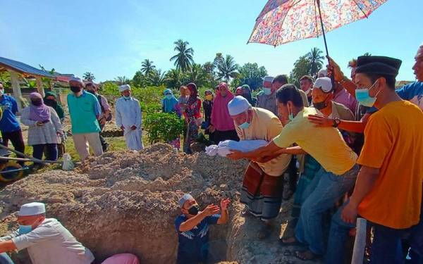 Mohd Khairi (dua dari kanan) menyerahkan jenazah bayinya untuk dikebumikan dalam satu liang lahad bersama isteri di Tanah Perkuburan Islam Kampung Banggol Stol, Repek Pasir Mas pada Sabtu.