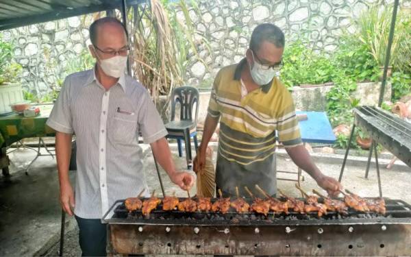 Hassan (kanan) ketika menyediakan ayam percik di rumahnya.