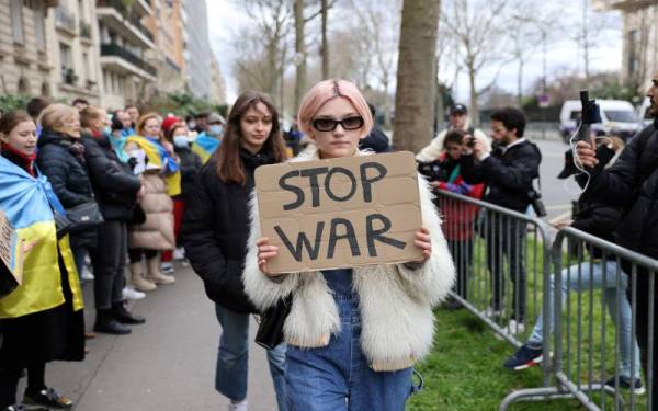 Seorang penunjuk perasaan memegang plakad tertera 'hentikan perang' ketika menyertai demonstrasi di hadapan Kedutaan Rusia di Paris pada Khamis. - Foto AFP