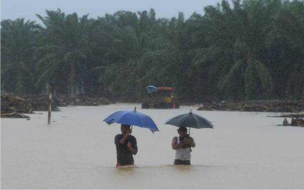 Dua pekerja ladang sawit meredah air banjir untuk ke jalan utama semasa tinjauan di Kampung Padang Kubu, Kemaman. - Foto Bernama 