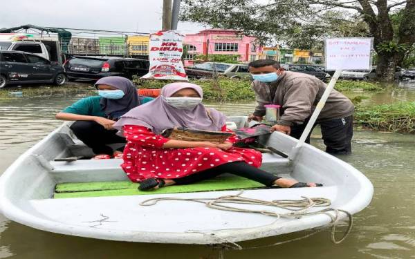 Penduduk dari Taman Sri Mas, Hunaizah Che Mat, 61, (tengah) berkata, dia bersyukur dengan adanya perkhidmatan bot tambang yang ditawarkan Mohd Irwani (kanan) memudahkan urusan mereka yang terperangkap akibat musibah banjir di Jalan Lubuk Jong, Pasir Mas ke Rantau Panjang di sini, pada Isnin. - Foto Bernama 