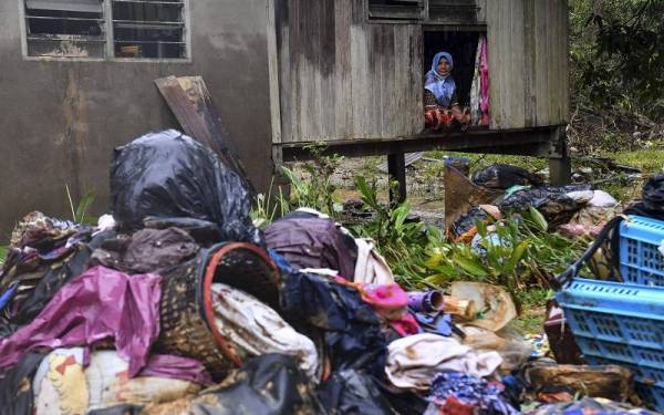 Timah termenung melihat serpihan dinding rumahnya yang tercabut akibat ditolak arus deras selepas kediamannya ditenggelami banjir di Kampung Bukit Gemuruh pada Jumaat. - Foto: Bernama