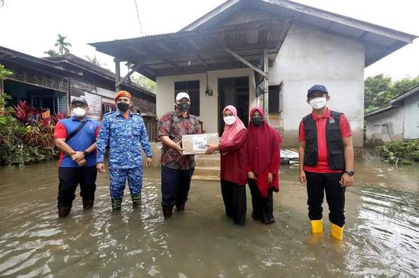 Dr Razli (tengah) dan kakitangan UMK lain turut meredah air sehingga paras lutut dan menggunakan bot untuk menyampaikan sumbangan pelajar berkenaan. 