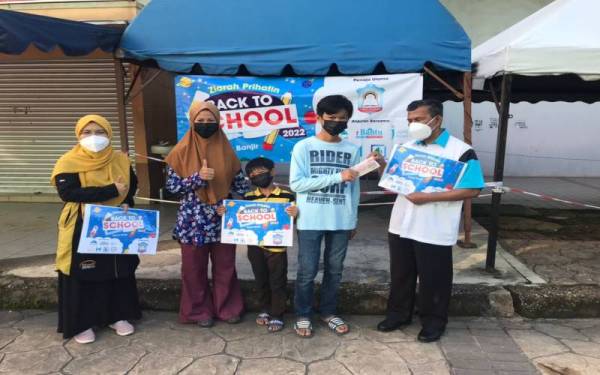 Karim (kanan) menyerahkan baucar kepada salah seorang penerima pada Program Ziarah Prihatin: Kembali Ke Sekolah 2022 di sebuah pasar raya di Kuantan pada Ahad.