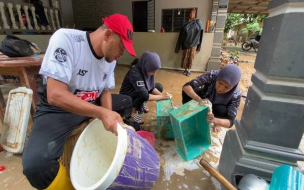 Che Mohd Zulkarnain (kiri) bersama atlet ragbi wanita bergotong royong membersihkan pinggan mangkuk dipenuhi lumpur di kediaman seorang mangsa banjir di Kampung Gunung, Menerong, Hulu Terengganu.