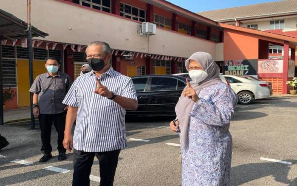 Muhyiddin (kiri) bersama Noorainee menunjukkan calitan ungu di jari masing-masing selepas selesai membuang undi di SMK Sri Muar, Muar pada Sabtu.