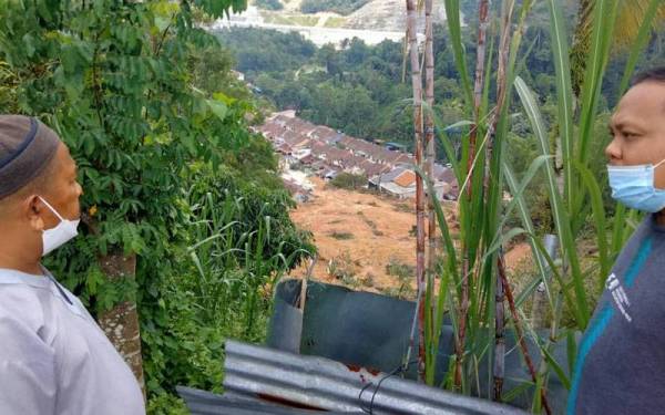 Mohd Faizal (kanan) bersama Mokhtar (kiri) yang datang melihat keadaan tanah runtuh di bahagian belakang rumahnya di Jalan Taman Permai 1.