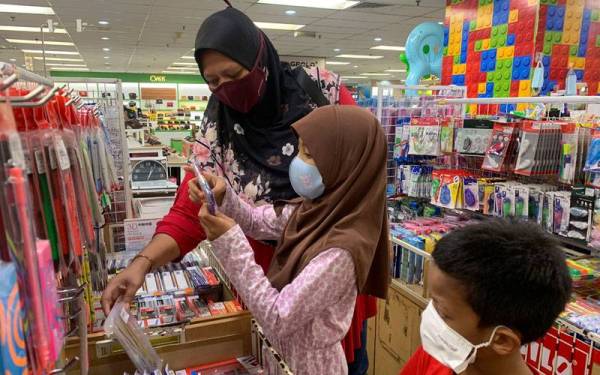 Azeanti (kiri) membawa anak-anaknya membeli peralatan sekolah di sebuah pasar raya di Kota Bharu, Kelantan pada Jumaat.