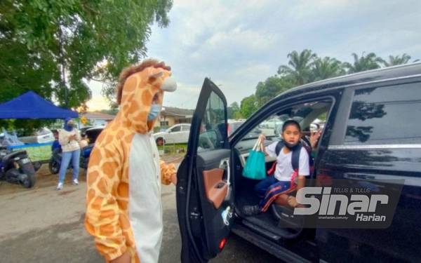 Mohd Shazreen (kiri) ketika menyambut salah seorang murid pendidikan khas SK Paya Rumput yang memulakan sesi persekolahan pada Isnin.