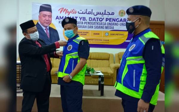 Hasnan (kiri) memakaikan jaket khas kepada anggota penguat kuasa yang akan menjalankan tugas mereka sepanjang Ramadan ini.