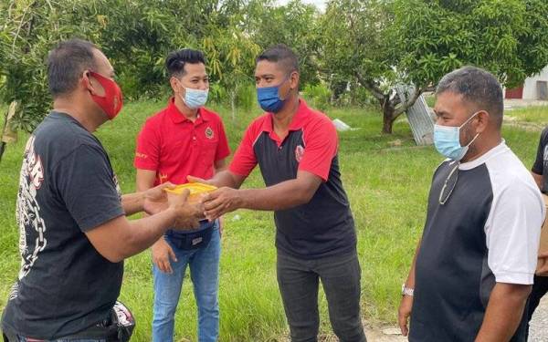 Khairul Nizam (dua dari kanan) bersama Hazdi (dua dari kiri) mengedarkan bubur lambuk kepada orang ramai di sekitar Kangar pada Sabtu.