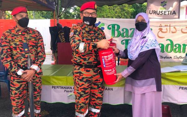 Zainal (tengah) menyerahkan alat pemadam api kepada Wan Nora (kanan) untuk kegunaan pihak pengurusan bazar di waktu kecemasan di Bazar Ramadan Stadium Sultan Muhammad IV, Kota Bharu pada Isnin.