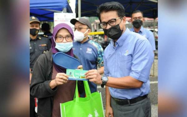 Johary (kanan) mengedarkan baucar RM5 kepada pelanggan yang membawa bekas makanan sendiri semasa lawatannya ke bazar Ramadan USJ 4, Subang Jaya pada Rabu.