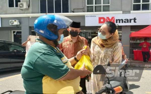 Azreen (kanan) menyerahkan sumbangan 'beg terkejut' kepada seorang penunggang motosikal di hadapan Kedai DMart Bukit Beruang di sini, pada petang Rabu.