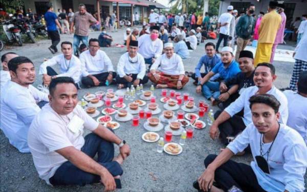 Asyraf Wajdi (enam dari kanan) duduk bersila di atas jalan tar sempena Iftar Ramadan anjuran Pemuda UMNO Kubang Pasu, yang menjadi amalan tradisi penduduk di Kampung Padang Gelam, Jitra pada Jumaat.