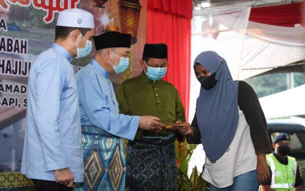 Hajiji (dua, kiri) menyampaikan sumbangan kepada salah seorang asnaf ketika hadir di Majlis Iftar Rakyat Bersama Masyarakat Batu Sapi, pada Sabtu. - Foto Bernama