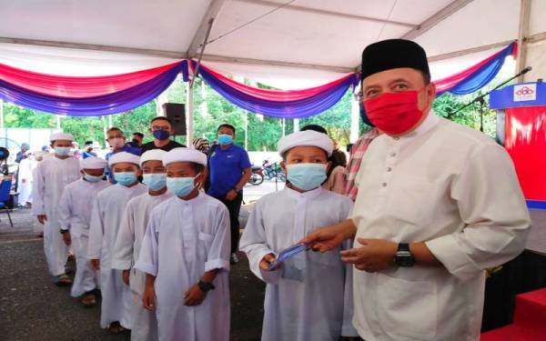 Ahmad Jazlan (kanan) menyampaikan zakat kepada penerima di Pusat Transformasi Ilmu, Bukit Tiu, Machang pada Selasa.