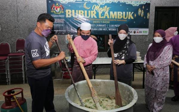 Dari kiri: Badrul Hisham, Nik Muhammad Zawawi dan Sartini Mohd Noor mengacau bubur lambuk dan diperhatikan oleh Habshah Ali.