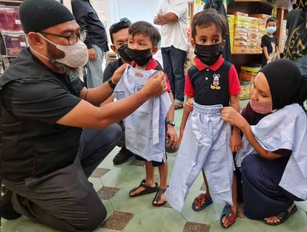 Asmadi (kiri) membantu memakai baju raya kepada salah seorang kanak-kanak daripada 35 penerima di gedung tekstil terkemuka di Bandaraya Kuantan pada Ahad.