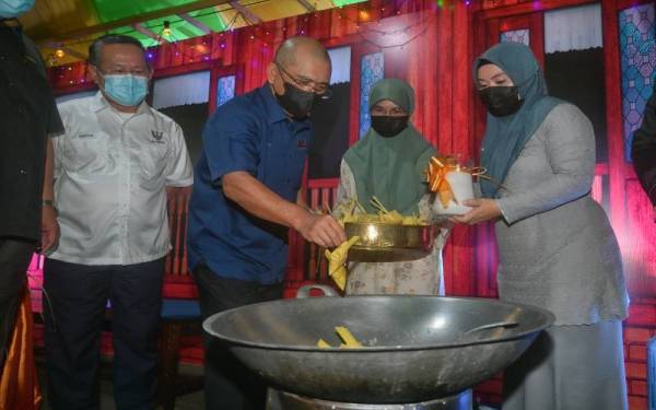 Ronald (dua dari kiri) mencuba bakat memasak ketupat sebagai gimik perasmian Majlis Semarak Syawal Peringkat Kebangsaan di Medan Niaga Satok, Kuching pada Ahad. - Foto Bernama