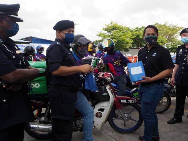 Amran (dua dari kiri) menyampaikan cenderamata kepada seorang penghantar makanan sempena Program Jelajah Op Selamat 18 dan Program 'Go To Safety Point' di Semabok pada Ahad.