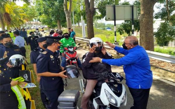 Mohd Zolkafly (kanan) menyarungkan topi keledar kepada penunggang motosikal pada Majlis Pelancaran Kempen Keselamatan Jalan Raya Sempena Sambutan Hari Raya Aidilfitri Negeri Perak di Plaza Tol Ipoh (U) arah selatan, pada Selasa.