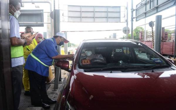 Che Had (dua dari kiri) mengedarkan cenderahati kepada pengguna lebuh raya di Plaza Tol Hutan Kampung di Alor Setar di sini pada Selasa.