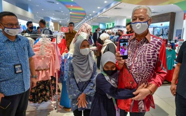 Ismail Sabri Yaakob dipeluk Nur Auni Syafia Jefri Mohd Zain, 11, sambil diperhatikan kakaknya, Nur Syamimi, 12, ketika menemani mereka membeli baju raya di sebuah pusat beli belah pada Khamis. - Foto Bernama 