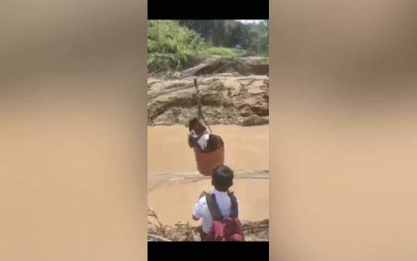 Tangkap layar video tular dua orang kanak-kanak berpakaian seragam sekolah melintasi sungai menggunakan tong drum yang ditarik menggunakan rel merintangi sebatang sungai di Sabah.