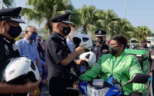 Mior Faridalathrash (dua dari kiri) memakaikan topi keledar baharu kepada salah seorang penunggang motosikal pada pelancaran Op Selamat 18 dan Kempen Keselamatan Jalan Raya sempena Hari Raya Aidilfitri Peringkat Perak di Ipoh pada Jumaat.