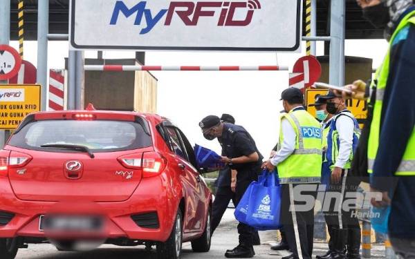 Ahmad Shukri (kiri) menyampaikan cenderahati sambil beramah mesra dengan pengguna lebuh raya yang masuk ke Alor Setar melalui Plaza Tol Alor Setar Selatan pada Jumaat.