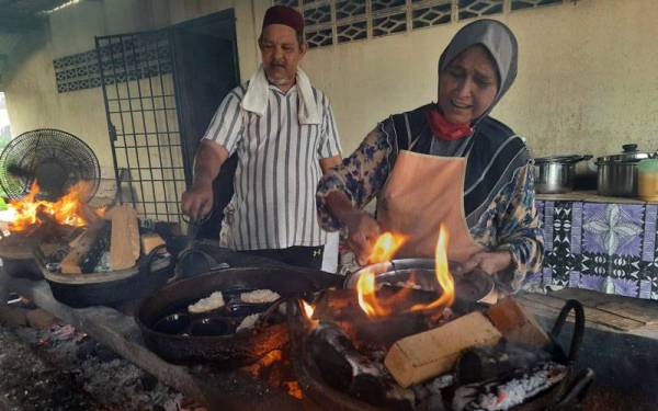 Khatijah (kanan) memasukkan aduan kuih bingka sebelum dibakar manakala anaknya, Suhairi Ahmad@ Abdul Hamid, 47, mengawal api bagi memastikan kuih masak sekata.