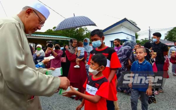 Ahmad (kiri) menyampaikan duit raya kepada kanak-kanak yang hadir pada majlis Rumah Terbuka Aidilfitri di rumahnya di Kampung Alor Pasir, Tumpat pada Rabu.