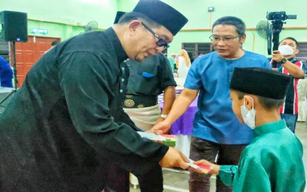 Muhammad Jailani (kiri) ketika menyampaikan duit raya kepada anak yatim ketika Majlis Rumah Terbuka Dewan Undangan Negeri (DUN) Rembia di Kompleks JAPERUN Rembia di sini, pada Jumaat.