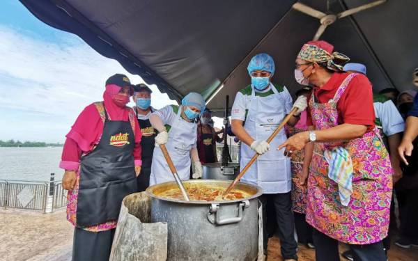 Nancy (tengah) bersama Ahmad Samsuri (dua dari kanan) mengacau gulai kawah ketika acara Rewang Raya sempena Majlis Rumah Terbuka Malaysia Aidilfitri 2022 di Masjid Kampung Seberang Takir, Kuala Nerus pada Jumaat.