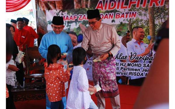 Mohd Salim (kanan) menyampaikan sumbangan duit raya kepada kanak-kanak yang hadir di Majlis Rumah Terbuka Aidilfitri 2022 Parlimen Jempol Bersama RISDA Malaysia, pada Jumaat.