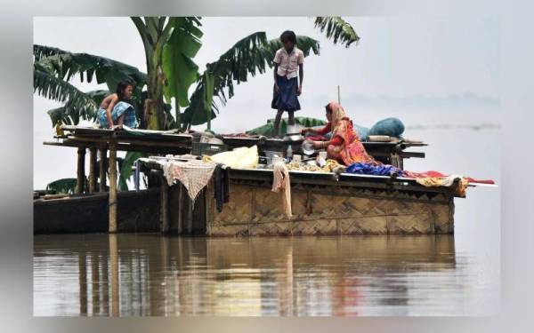 Sebuah keluarga berada di atas atap rumah untuk mendapatkan perlindungan susulan banjir melanda di Assam, India dan setakat ini situasi tersebut belum menunjukkan tanda akan reda. - Foto AFP