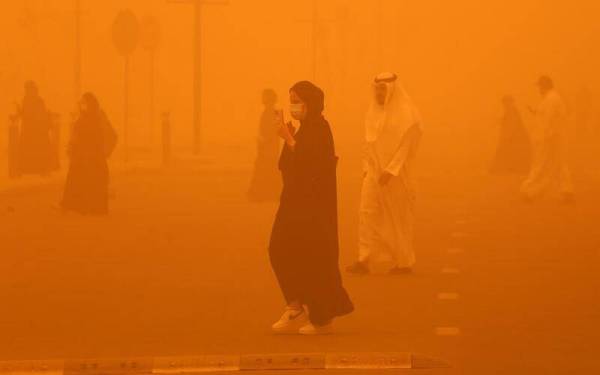 Orang ramai bersiar-siar ketika keadaan sekeliling di Kuwait City bertukar jingga akibat ribut pasir. - AFP