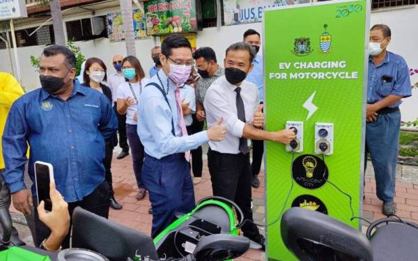 Zairil (dua dari kiri) bersama Tung Seang menunjukkan stesen pengecas motosikal elektrik percuma di Medan Renong, Padang Kota Lama pada Selasa.