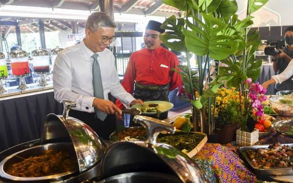 Tengku Zafrul mengambil juadah diiringi Presiden Kelab Media Putrajaya Wan Zairul Azri Wan Mohammad Sudin pada majlis Rumah Terbuka Kelab Media Putrajaya pada Rabu. - Foto Bernama