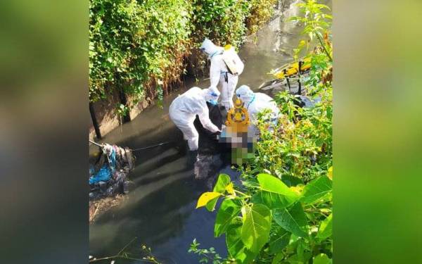 Anggota bomba ketika menjalankan kerja membawa keluar mayat berkenaan dari longkang tersebut. - Foto Bomba