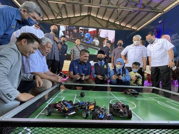 Radzi (duduk berbaju biru) bersama Idris (duduk berbaju putih) mencuba permainan robotik yang dihasilkan oleh pelajar Sekolah Kebangsaan Sahabat 4, Lahad Datu pada Sabtu.