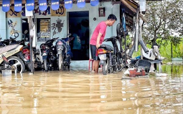 Mohd Fadhlan menolak motosikal pelanggan yang di depan bengkel di Kampung Paya Rumput, Tangga Batu, di sini, pada Khamis.