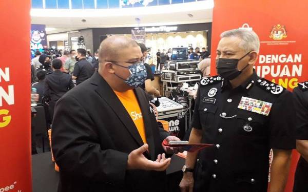 Acryl Sani (kanan) diberi penerangan berkenaan pencegahan jenayah semasa melawat reruai selepas melancarkan Kempen Anti Scam PDRM 2022 di Mid Valley South Key, Johor Bahru pada Sabtu.